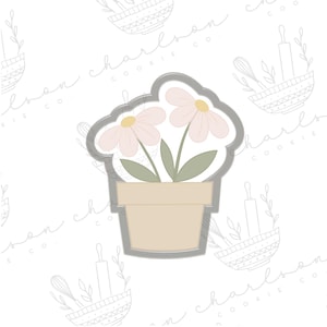 Może przedstawiać: Wycinarka do ciasteczek w kształcie doniczki z dwoma różowymi kwiatami. Wycinarka jest wykonana z metalu i ma jasnoszary kolor.