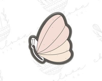 May include: A pink and beige butterfly cookie cutter with a detailed outline. The cutter is made of metal and has a smooth finish.