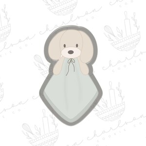 May include: A gray cookie cutter shaped like a dog wearing a light blue blanket. The cookie cutter is designed for baking and decorating cookies.