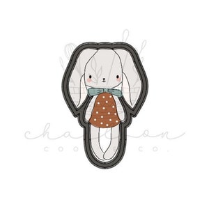 May include: A black and white cookie cutter in the shape of a bunny wearing a brown and white polka dot dress and a blue bow.