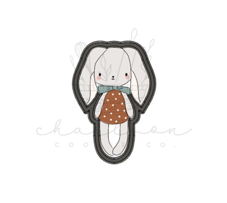 May include: A black and white cookie cutter in the shape of a bunny wearing a brown and white polka dot dress and a blue bow.