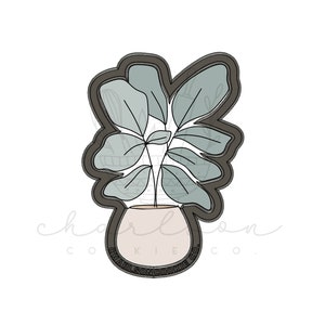 Pode incluir: Um cortador de biscoitos preto em forma de planta em vaso com um único caule e folhas. As folhas são de cor verde claro e o vaso é de cor marrom claro. O cortador de biscoitos é rotulado como "Charlson Cookie Co."
