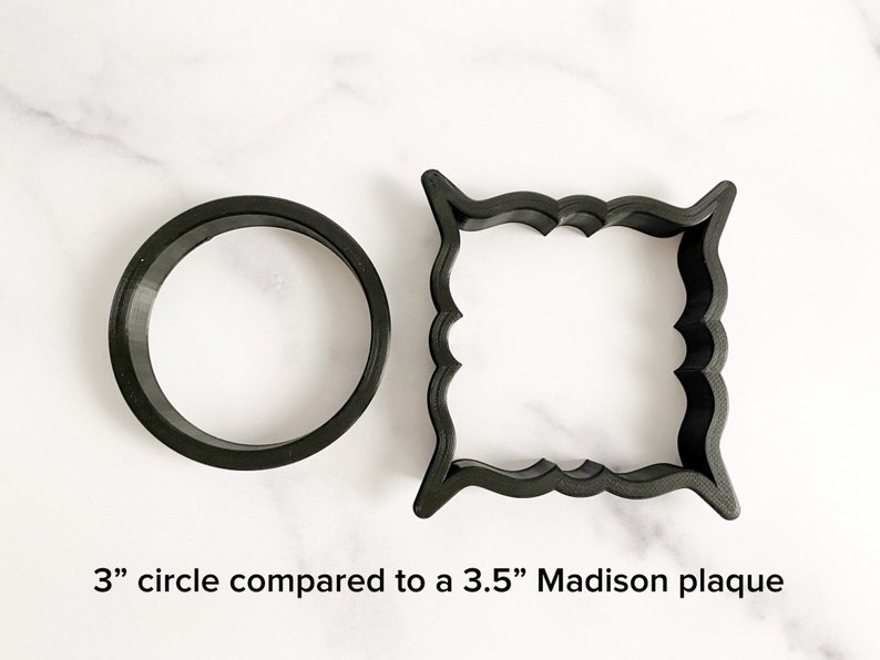 May include: A comparison of two cookie cutters: a 3-inch circle and a 3.5-inch Madison plaque. Both cutters are black and made of plastic.