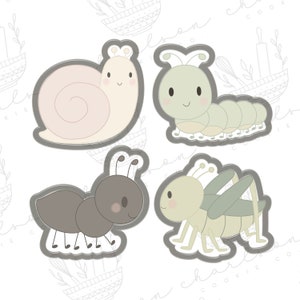May include: Four cookie cutters in the shape of cute insects. The set includes a snail, caterpillar, ant, and grasshopper. Each insect has a smiling face and is outlined in gray.