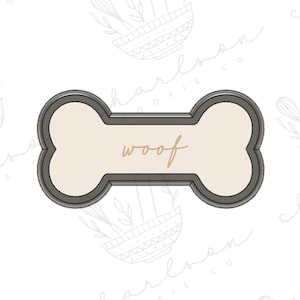 May include: A gray metal cookie cutter shaped like a dog bone with the word "woof" written in brown on the inside.