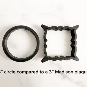 May include: A comparison of two cookie cutters: a 3-inch circle and a 3-inch Madison plaque. Both are black and made of plastic.