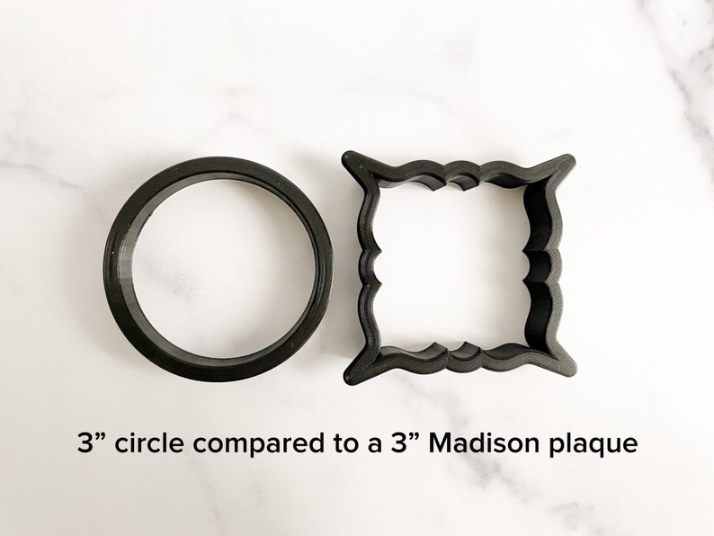 May include: A comparison of two cookie cutters: a 3-inch circle and a 3-inch Madison plaque. Both are black and made of plastic.