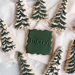 May include: A collection of green and white decorated sugar cookies shaped like Christmas trees and a sign that says "merry".