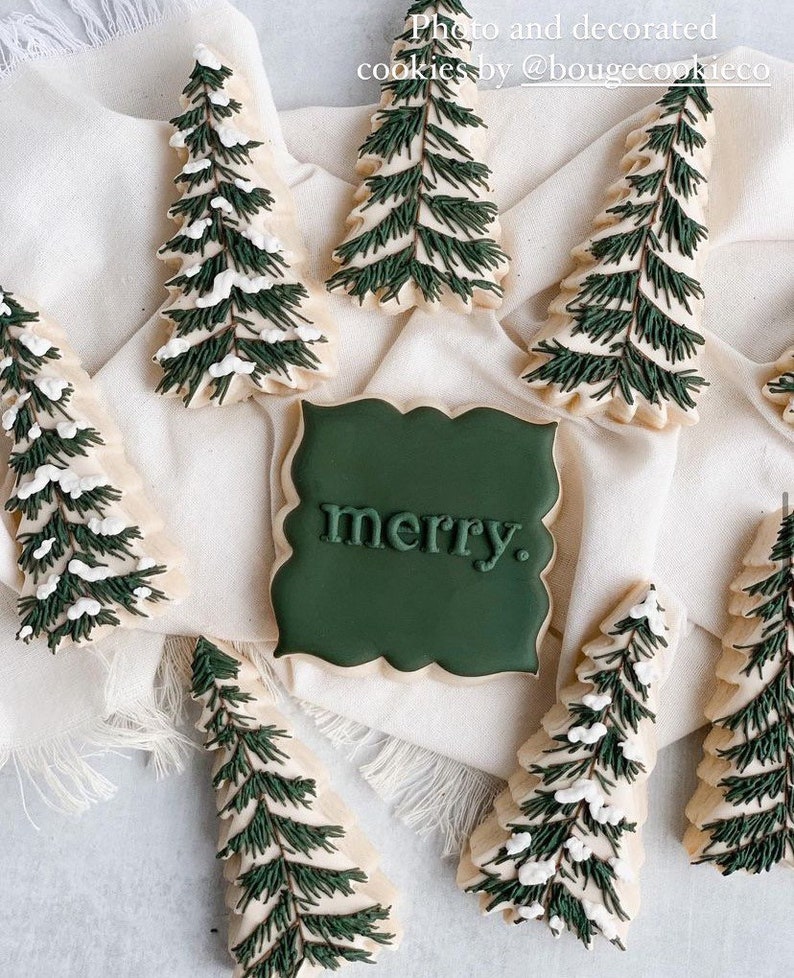 May include: A collection of green and white decorated sugar cookies shaped like Christmas trees and a sign that says "merry".