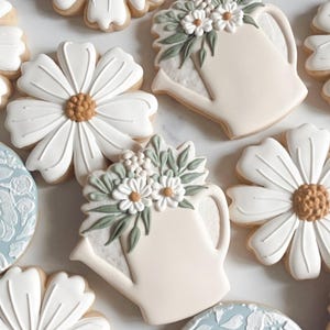 May include: Assortment of decorated sugar cookies featuring floral designs and a watering can with flowers. The cookies are white with green and brown accents.