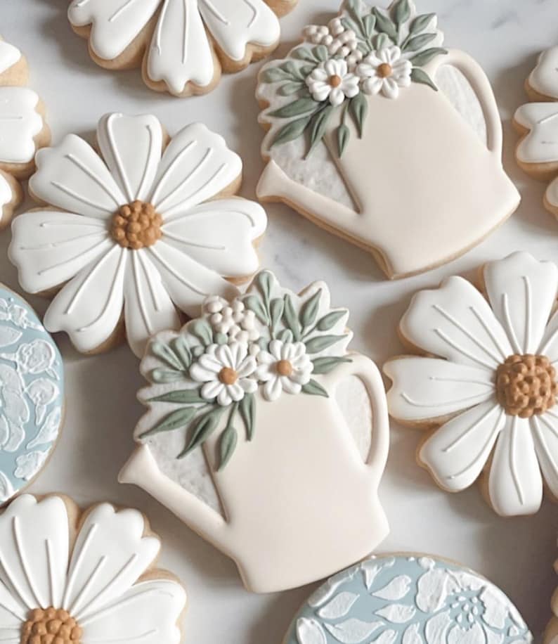 May include: Assortment of decorated sugar cookies featuring floral designs and a watering can with flowers. The cookies are white with green and brown accents.