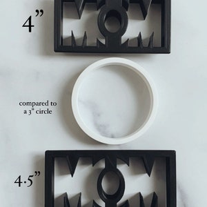 May include: Two black plastic cookie cutters shaped like the word "MOM". The top cutter is 4 inches wide and the bottom cutter is 4.5 inches wide. The cutters are shown next to a white plastic circle, which is 3 inches in diameter.