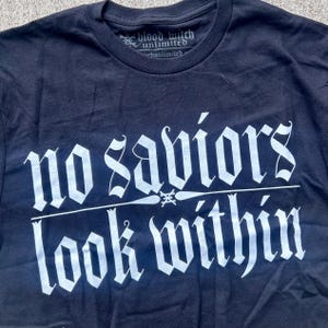 May include: Black t-shirt with the text "no saviors look within" in white gothic lettering. The shirt also features the text "blood witch unlimited" at the neckline.