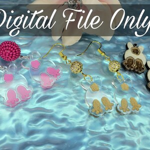 May include: Three pairs of dangle earrings with different charms. The first pair features pink beads and clear plastic charms with pink paw prints. The second pair features clear plastic charms with gold glitter and gold paw prints. The third pair features wooden charms of a dog with brown and white fur.