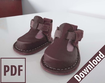 May include: A pair of burgundy leather baby shoes with a strap and buckle closure. The shoes have a pink lining and a white stitch detail around the sole.  PDF Download.