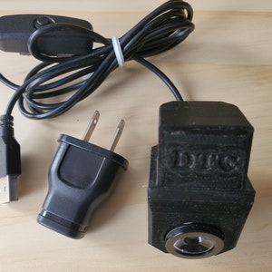 Puede incluir: Una luz LED negra alimentada por USB con un adaptador de corriente y un interruptor de encendido/apagado. La luz tiene una lente transparente y la palabra "DIYC" est&aacute; impresa en el lateral.