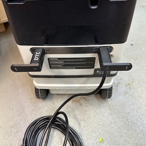 May include: A black and white vacuum cleaner with a black power cord. The vacuum has two black handles with the letters "DTC" on them. The vacuum cleaner has wheels and a warning label.
