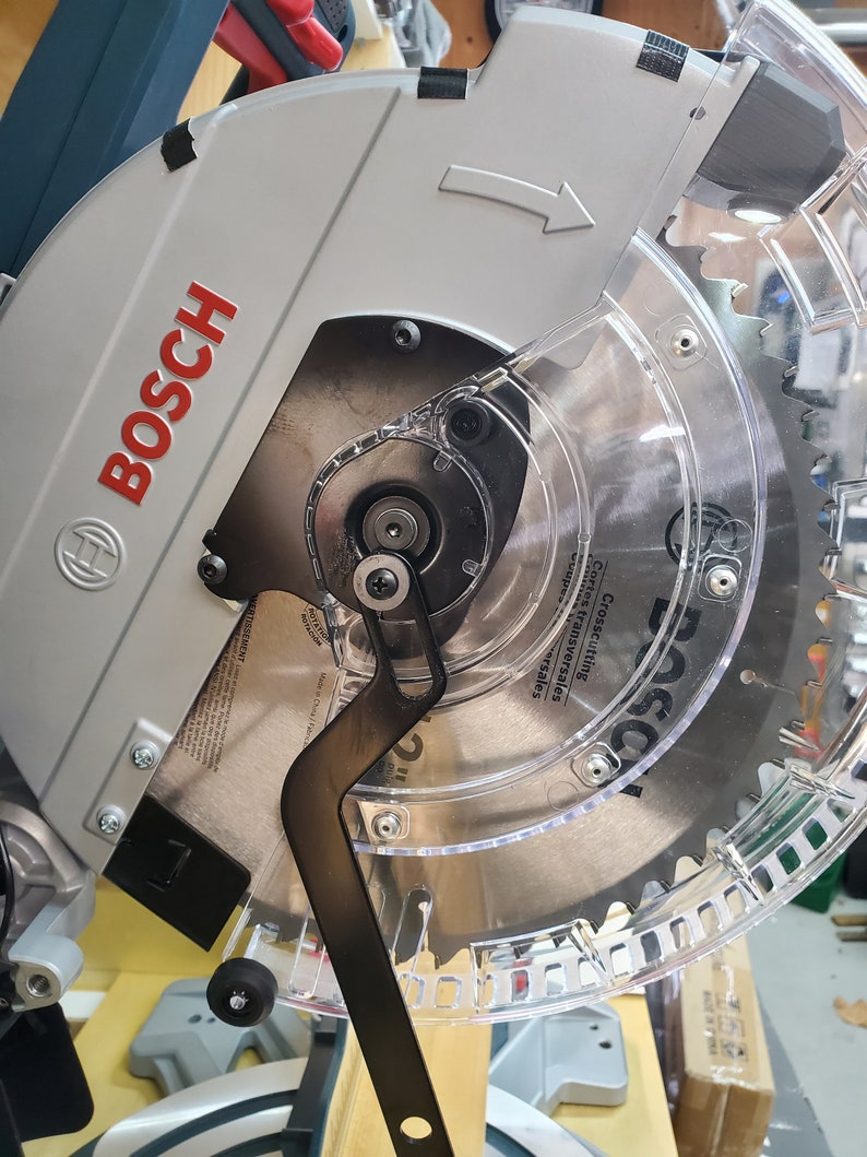 Puede incluir: Primer plano de una sierra circular Bosch plateada y negra con una protecci&oacute;n de pl&aacute;stico transparente. La sierra tiene un mango negro y una hoja plateada. La hoja est&aacute; etiquetada con "Bosch" y "Crosscutting,  Compound,  and  Transversales".