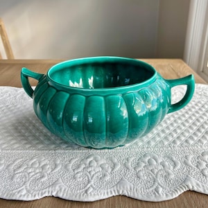 May include: A large, green ceramic bowl with two handles. The bowl has a fluted design and a glossy finish.