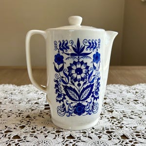 May include: White ceramic pitcher with a blue and white floral design. The pitcher has a lid and a handle.