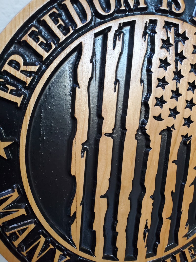 K&ouml;nnte beinhalten: Ein Holzschild mit einem schwarz-wei&szlig;en amerikanischen Flaggenmuster. Das Schild lautet "Freiheit ist nicht frei".