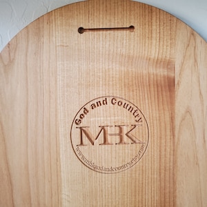 K&ouml;nnte beinhalten: Ein rundes Holzschild mit einem kreisf&ouml;rmigen Logo, auf dem "God and Country" steht, mit den Initialen "MHK" im Kreis. Das Logo enth&auml;lt auch die Website "www.godandcountryetsy.com".
