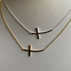 May include: Two delicate necklaces with a curved bar and cross pendant. One necklace is gold and the other is silver.