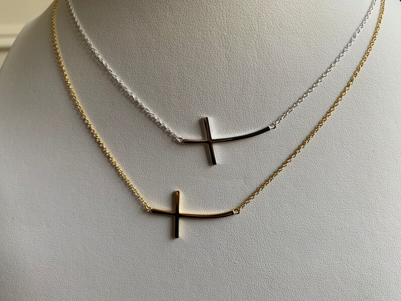 May include: Two delicate necklaces with a curved bar and cross pendant. One necklace is gold and the other is silver.
