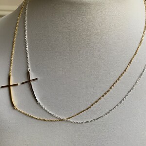 May include: A layered necklace with two chains, one gold and one silver, featuring a sideways cross pendant on each chain.