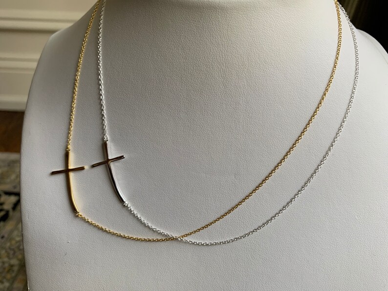 May include: A layered necklace with two chains, one gold and one silver, featuring a sideways cross pendant on each chain.