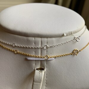 May include: Two necklaces on a white mannequin bust. The top necklace is silver and the bottom necklace is gold.