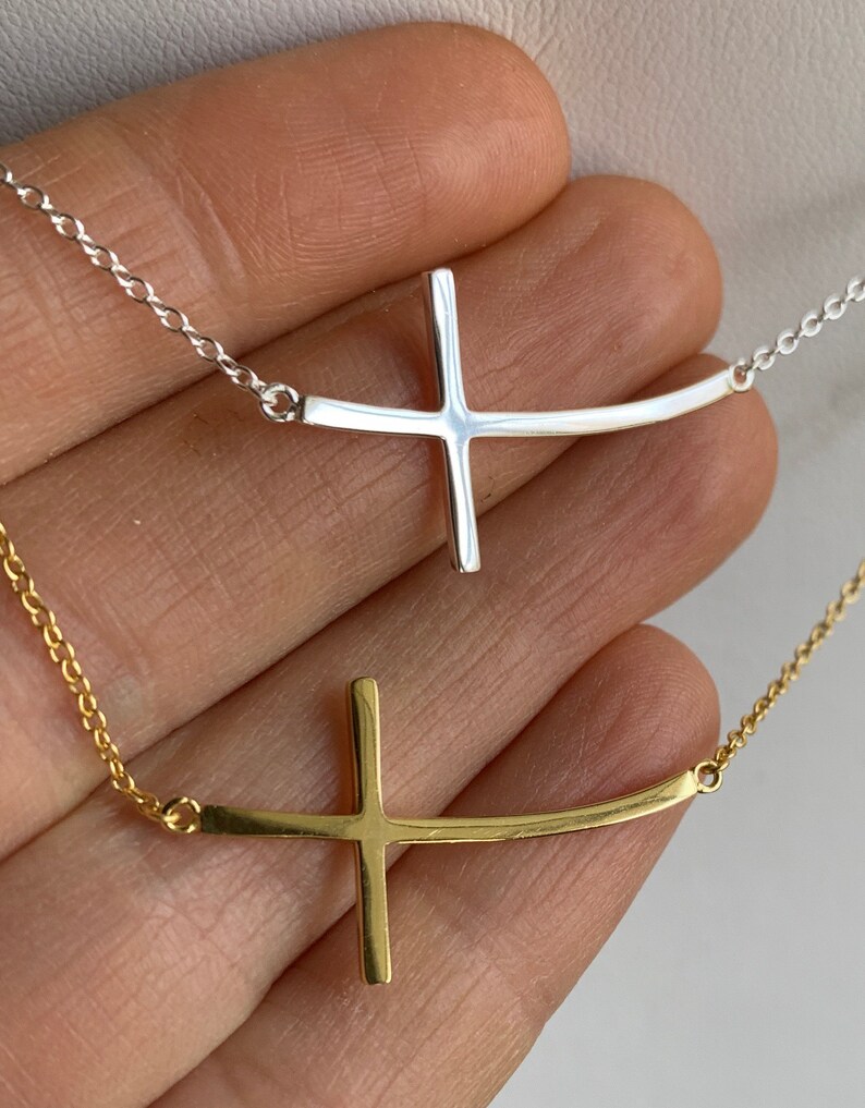 May include: Two delicate necklaces with a sideways cross pendant. One necklace has a silver chain and pendant, the other has a gold chain and pendant.