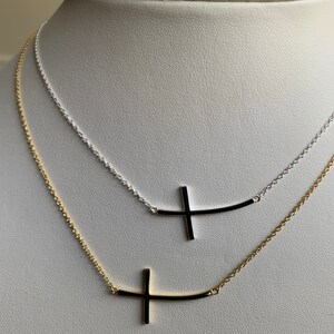 May include: Two delicate necklaces with a sideways cross pendant. The top necklace is silver and the bottom necklace is gold.