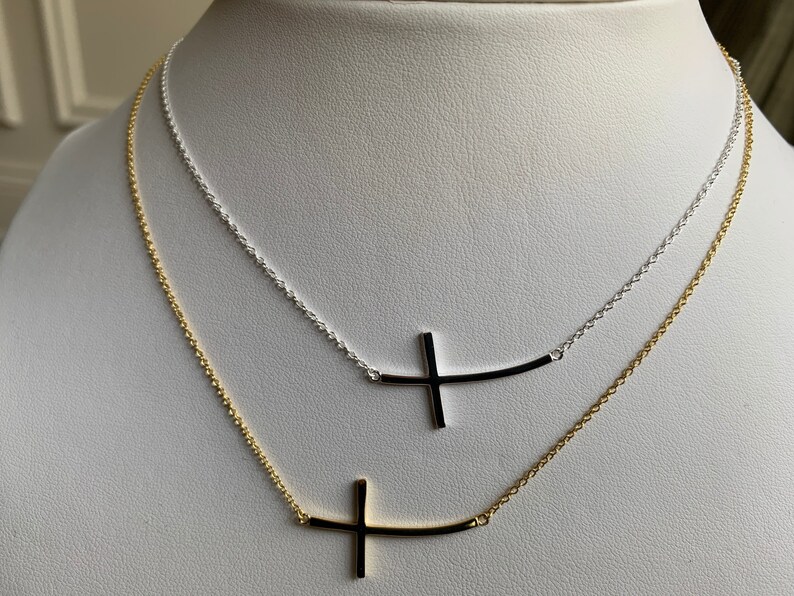 May include: Two delicate necklaces with a sideways cross pendant. The top necklace is silver and the bottom necklace is gold.