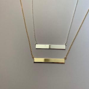 May include: Two delicate necklaces with bar pendants. One necklace has a silver bar pendant and the other has a gold bar pendant.
