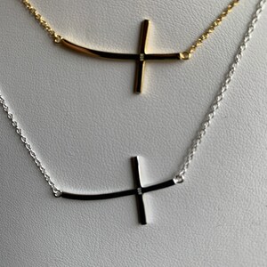 May include: Two delicate necklaces with a curved cross pendant. One necklace is silver and the other is gold.