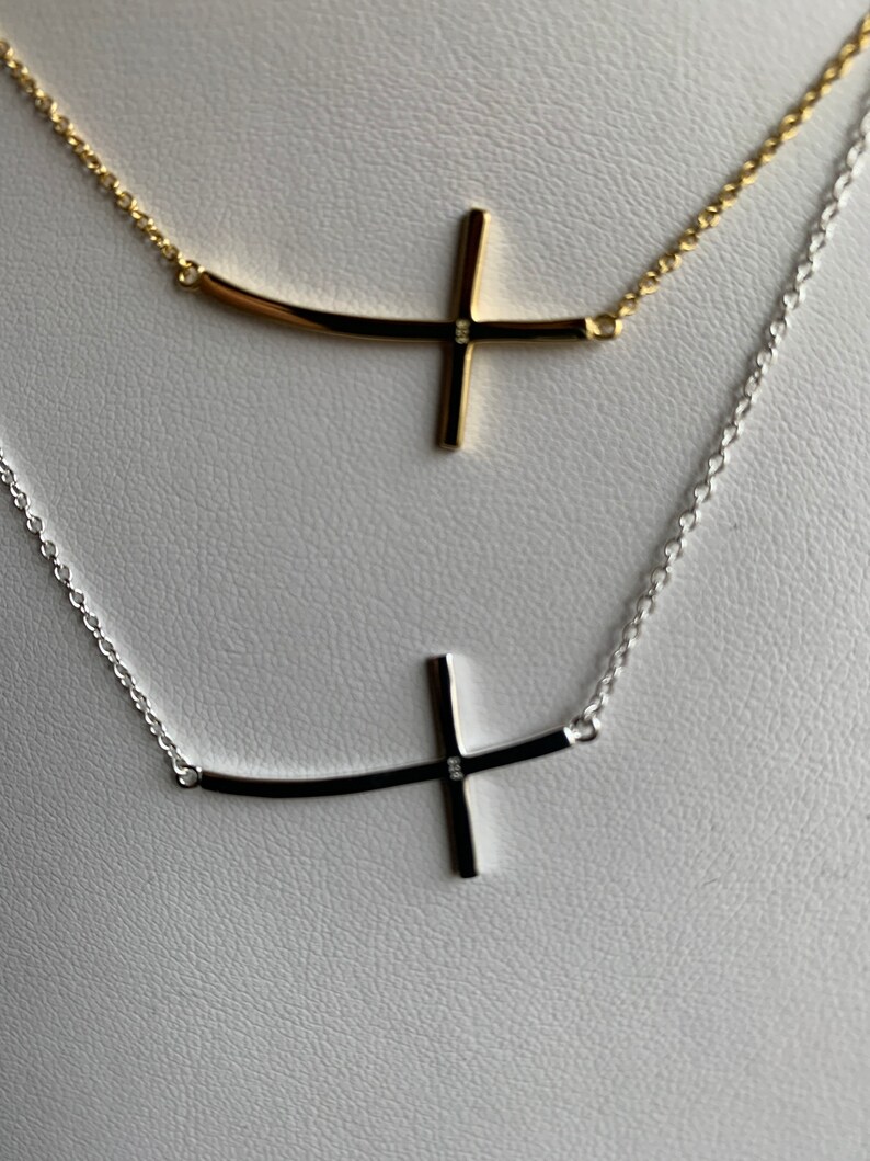 May include: Two delicate necklaces with a curved cross pendant. One necklace is silver and the other is gold.