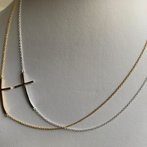 May include: A gold and silver chain necklace with two cross pendants. The cross pendants are made of metal and are in the shape of a cross. The necklace is on a white background.
