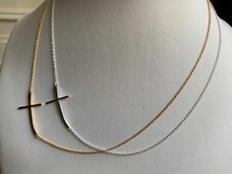 May include: A gold and silver chain necklace with two cross pendants. The cross pendants are made of metal and are in the shape of a cross. The necklace is on a white background.