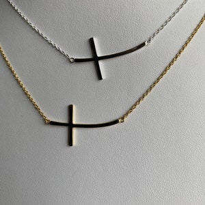 May include: Two delicate necklaces with a curved bar and a cross pendant. The top necklace is silver and the bottom necklace is gold.