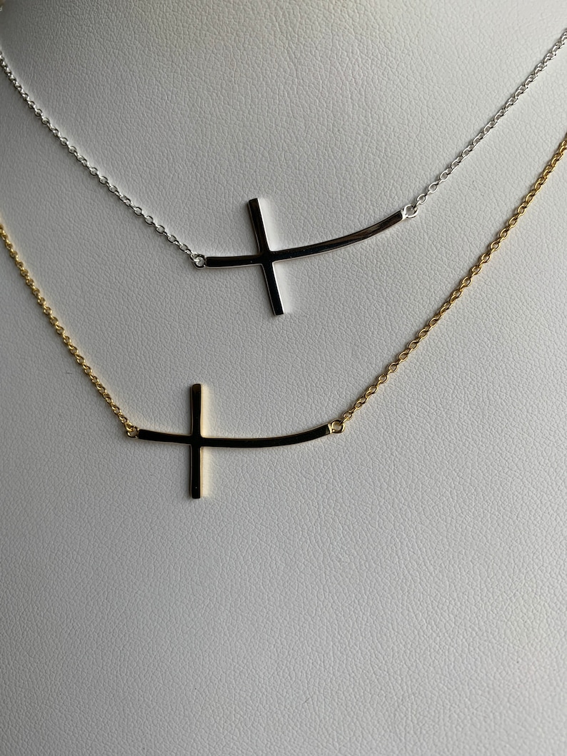May include: Two delicate necklaces with a curved bar and a cross pendant. The top necklace is silver and the bottom necklace is gold.
