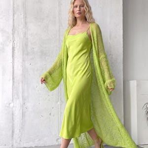 May include: A lime green midi-length slip dress with a cowl neckline and thin spaghetti straps, paired with a matching lime green open-front long-sleeve cardigan made of a sheer, lightweight knit fabric with wide, loose-fitting sleeves.