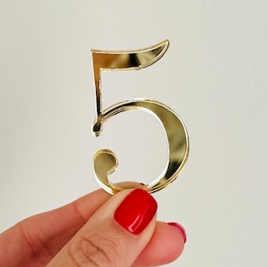 May include: Gold mirror-like number five, held in a hand with red nail polish.