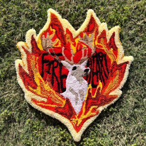 May include: A heart-shaped rug with a white deer in the center, surrounded by flames in shades of red, orange, and yellow. The text "FIRE HEART" is written around the deer.