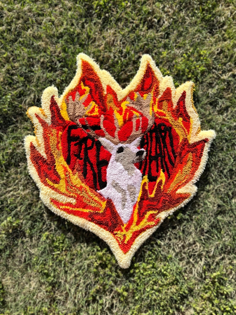 May include: A heart-shaped rug with a white deer in the center, surrounded by flames in shades of red, orange, and yellow. The text "FIRE HEART" is written around the deer.