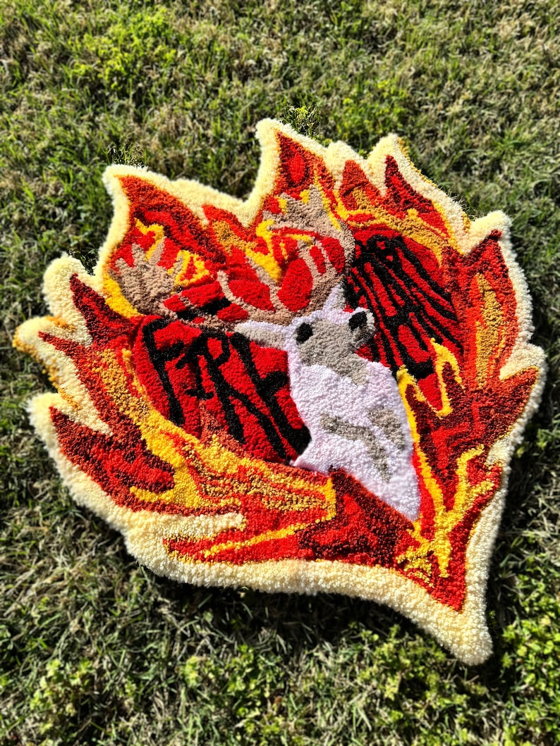 May include: A red, yellow, and white rug with a deer head in the center. The deer head is surrounded by flames. The rug is made of yarn and has a fluffy texture.