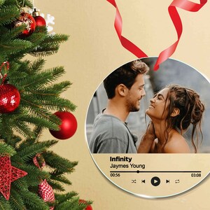 Peut inclure: Ornement rond en verre avec une photo d'un couple se regardant. L'ornement a une interface de lecteur de musique avec le titre de la chanson "Infinity" de Jaymes Young et une minuterie affichant 00:56 &agrave; 03:08.