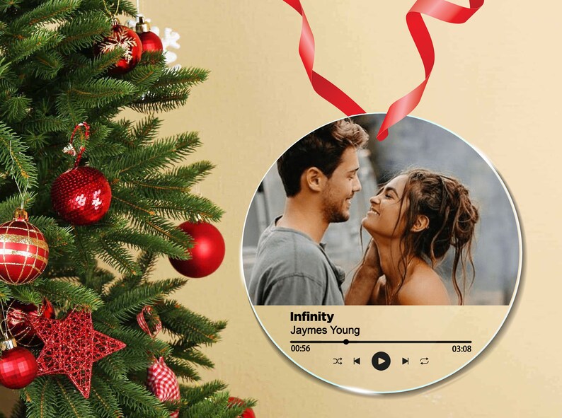 Peut inclure: Ornement rond en verre avec une photo d'un couple se regardant. L'ornement a une interface de lecteur de musique avec le titre de la chanson "Infinity" de Jaymes Young et une minuterie affichant 00:56 &agrave; 03:08.
