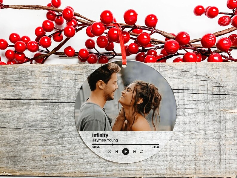Peut inclure: Une boule de No&euml;l ronde et argent&eacute;e avec une photo d'un couple se regardant. La boule a un design de lecteur de musique avec le titre de la chanson "Infinity" de Jaymes Young.