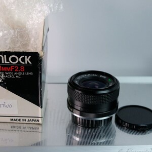 May include: A black Kenlock 28mm f/2.8 automatic wide angle lens with macro and multi-coated optics. The lens is in its original box, which is white with black text. The box says "Kenlock 28mmF2.8 Automatic Wide Angle Lens with Macro, MC. Objetivo Made in Japan."